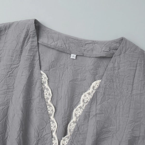 Détail du col en V avec dentelle blanche et texture de tissu gris plissé sur la robe