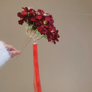 Close-up of red fabric flowers and golden U-shaped hair fork with long silk ribbon