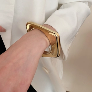 Close-up of a wide geometric golden bangle styled with a white blazer for a chic look