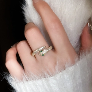 Close-up of gold snake ring with white cubic zirconia and green stone eyes on hand