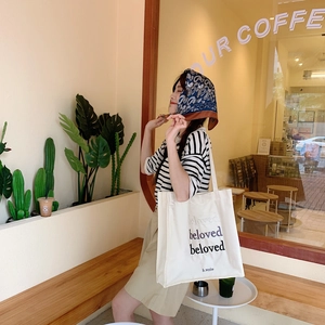 Détail du sac cabas en toile blanche avec broderie 'beloved' dans un décor de café