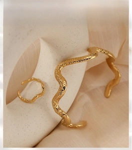 Detailed view of gold wave textured bracelet and ring set on ceramic display