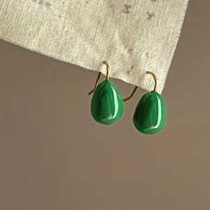 Detail of green teardrop enamel earrings with gold hooks on textured cream fabric