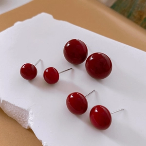 Detailed view of three pairs of glossy red round stud earrings in various sizes on a pedestal