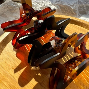 Three wave-shaped hair claw clips in amber and black colors on a wooden tray