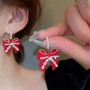 Dettaglio di orecchini a fiocco in velluto rosso con perle e strass su donna