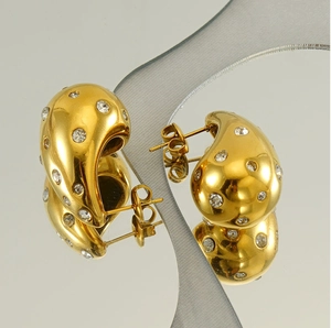 Macro view of 18K gold teardrop earrings with crystal pavé on a reflective mirror