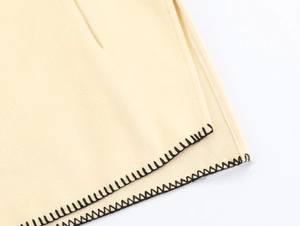 Detail of beige wool coat with contrasting black blanket stitch along the fabric edge