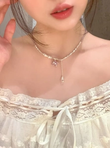 Primo piano di una collana con farfalla in zircone viola e perle su una clavicola.