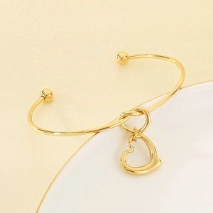 Detailed macro view of 18K gold plated heart charm on minimalist open bangle bracelet