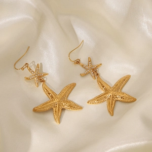 Macro detail of gold-plated starfish earrings with white zircons on cream silk background