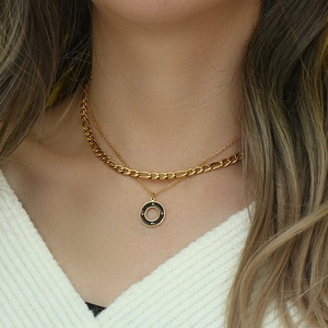 Close-up of a layered gold necklace featuring a black circular pendant with star motifs
