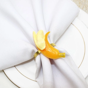 Detail of yellow banana napkin ring on white fabric and gold-rimmed plate