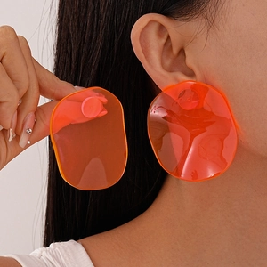 Detailed view of oversized transparent orange resin oval earrings worn by a model