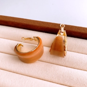 Détail de boucles d'oreilles créoles en résine ambre et bord doré sur plateau velours