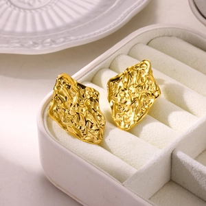 Detailed macro view of gold petal earrings with unique lava texture on white velvet box