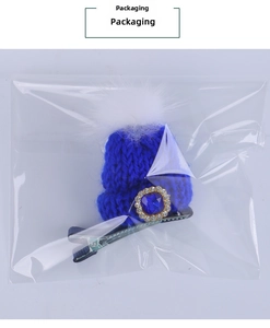 Blue knitted mini hat hair clip with pompom and faux gem in clear packaging detail