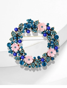 Dettaglio di una spilla a ghirlanda dorata con fiori rosa e cristalli blu brillanti