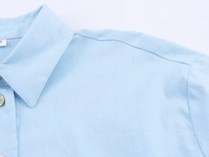Close-up of light blue linen shirt collar and buttons with fine fabric texture details