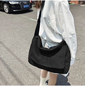 Outdoor shot of a black canvas messenger bag worn by a model in a casual urban setting
