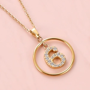 Macro shot of gold-plated pendant featuring a crystal-encrusted number 6 on a fine chain