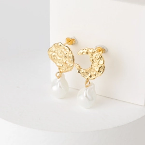 Detail of gold-plated irregular baroque pearl earrings with textured metal on a white pedestal