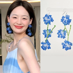Détail de boucles d'oreilles fleuries faites main en cristaux bleus et verts portées