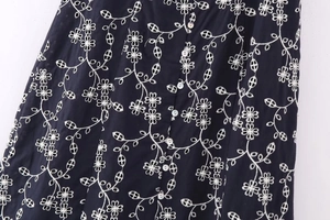 Detailed close-up of white floral embroidery and buttons on dark midi dress fabric