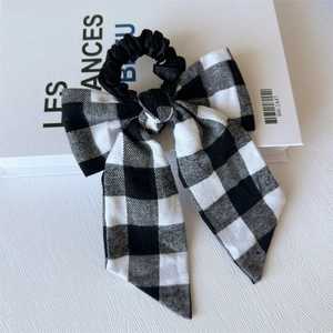Detail of a black and white checkered bow hair tie with satin band on a desk