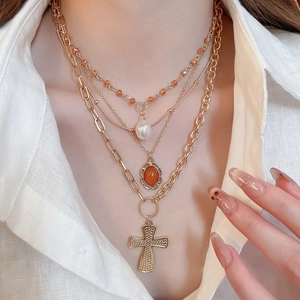 Detail of layered gold necklaces with acrylic pearl, orange stone, and cross pendant