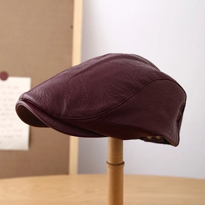 Classic dark red leather beret cap for women with premium texture on a wooden stand