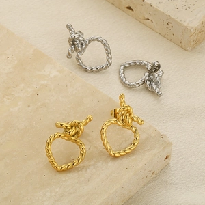 Détail de boucles d'oreilles nœuds tressés or et argent sur pierre beige