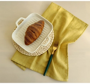 Close-up of a white rectangular ceramic plate with a yellow cotton napkin and straw mat