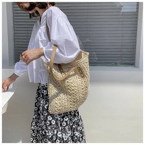 Close-up of beige woven straw tote bag with brown leather straps and cross-stitch detail