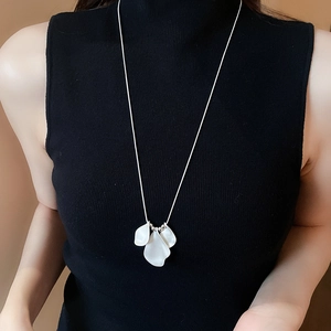 Detail view of a long petal pendant necklace worn over a black turtleneck top