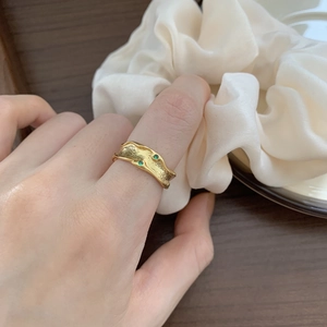 Detail of irregular wave gold ring with green gemstones on model's finger