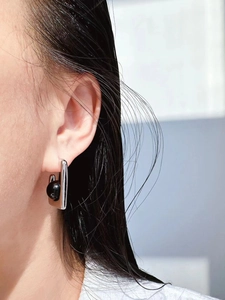 Detail view of geometric silver earrings with black onyx beads on a model's ear