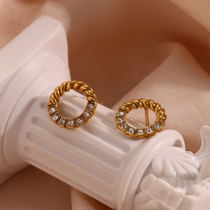 Macro shot of gold twisted hoop earrings with sparkling zircon crystals on a stone pillar
