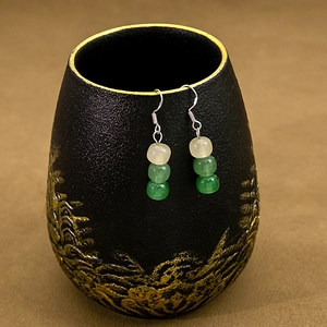 Detail of beaded water drop earrings with green beads on a black ceramic stand