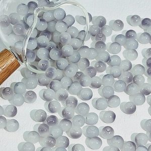 Close-up of 8mm grey and white gradient glass beads spilling from a glass beaker
