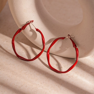 Detailed view of glossy red twisted geometric hoop earrings on a ceramic display
