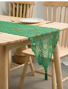 Detail of dark green lace table runner featuring fringe tassels and hollow knit patterns