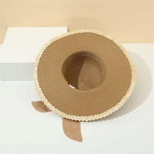 Close-up of wide brim straw hat with decorative bow and beige scalloped edge texture