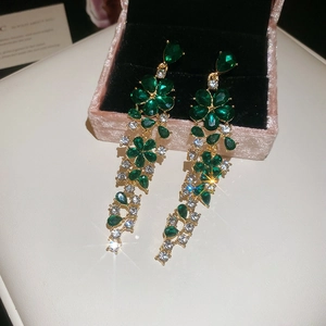 Close-up of elegant flower earrings with green rhinestones and long gold tassels