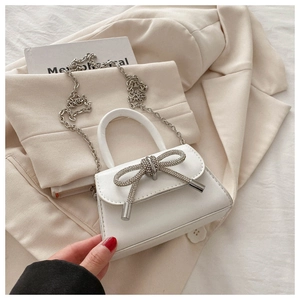 Detail showing the white mini bag with a rhinestone bow and silver chain strap