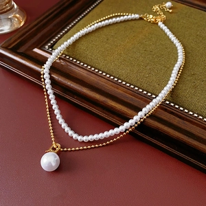 Detail of layered gold-plated necklace featuring white pearls on green velvet background