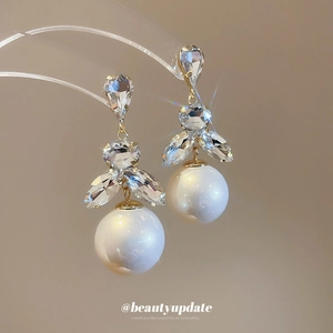 Vintage gold stud earrings with sparkling crystals and large white pearls on a stand