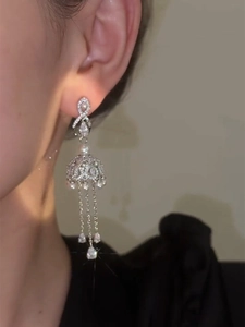 Macro shot of silver bow earrings with zircon tassels and water drop pearls worn by a model