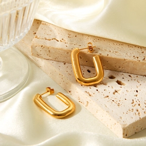 Polished gold U-shaped chunky stainless steel earrings on a textured stone surface