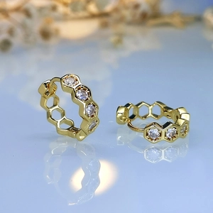 Macro view of gold honeycomb earrings with hexagonal zircons on a blue surface